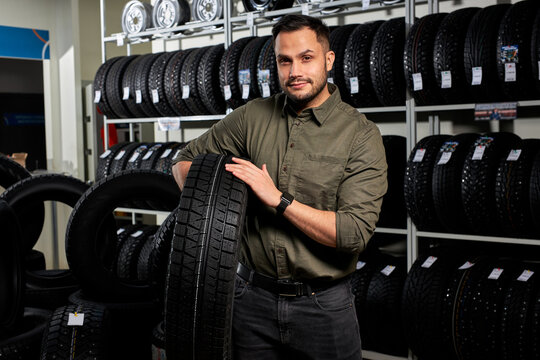 Client Guy Stands With Tires By Rack Of Tires, He Made Choice, Buy The Best Ones In Auto Service Shop. Portrait