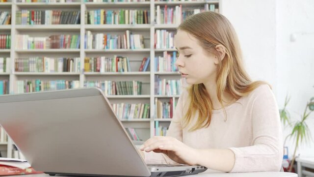 Charming teen girl working on her computer at the library. Teenage female student using laptop at public library. Knowledge, exams preparation concept