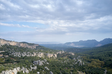 Summer nature scenery in mountains. Rocky cliffs over the grassy valley. Cloudy sky in the background.