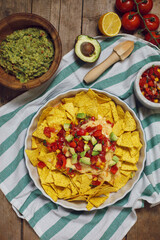 a plate of nachos with vegetables, avocado guacamole and cheese on a wooden surface. summertime dish