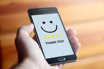 Male hand holding mobile phone with smiling happy face and five stars rating with the text 
