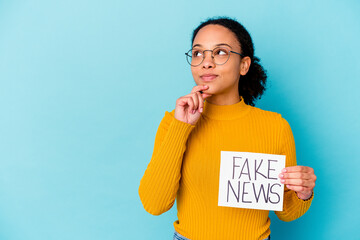 Young african american mixed race woman holding a fake news concept looking sideways with doubtful...