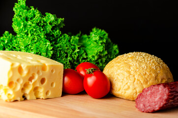 Making a sandwich from different ingredients from different ingredients. Cheese, sausage, salad and tomatoes on a dark background