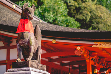 Fox (kitsune) stone statue wit red scarf at Fushimi Inari taisha shrine entrance stairs, Kyoto - Powered by Adobe
