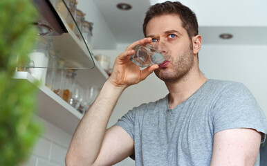 Fototapeta na wymiar Unshaven man drinks water from a glass in the kitchen.