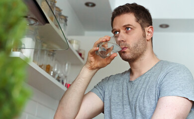 Fototapeta na wymiar Unshaven man drinks water from a glass in the kitchen.