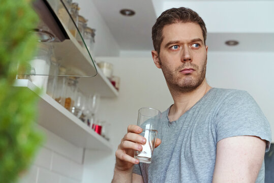 Unshaven man in the kitchen with a glass of water.
