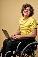 man disabled student preparing for exam using laptop, sitting on wheelchair isolated in studio....