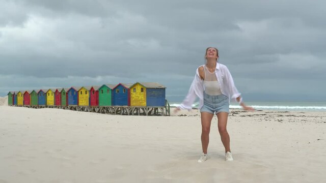 A girl dancing on the white sands of South Africa near the colorful wood Muizenberg Beach Houses.