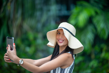 Asian business woman wearing straw hat visiting city taking selfies with smartphone