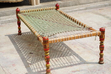 Photo of full desi charpaie indian pakistani traditional bed with red legs and woven rope in village.