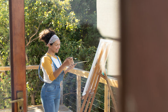 Smiling caucasian woman painting picture standing on sunny terrace