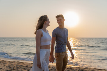 Young happy couple walking on the beach during sunset