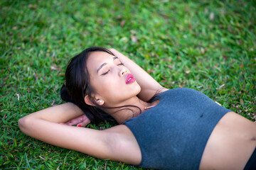 Naklejka na ściany i meble Beautiful asian girl lying down on the grass relaxing in the city park