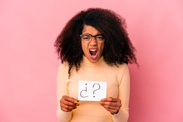 Young african american curly woman holding an interrogation on a placard screaming very angry and aggressive.