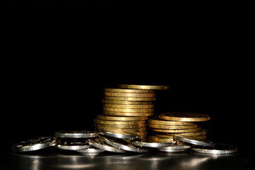 Stack of golden coins and heap of silver coins on a black background