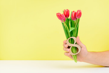 Bouquet of pink tulips in a male hand on a yellow background. Greeting card template with copy space. The concept of the holiday on March 8, Women's Day, Valentine's Day, mother's day