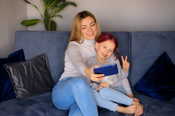 Happy family of cute little child daughter sit on the lap of parents mom on the couch to laugh and have fun with your smartphone