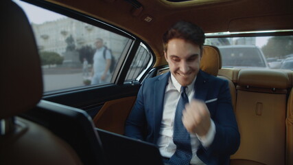 Happy business man exciting with good results of work on laptop in luxury car.