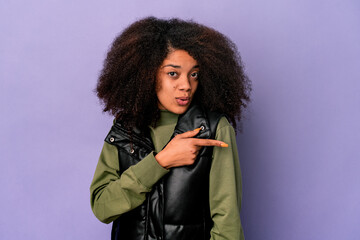 Young african american curly woman isolated on purple background smiling and pointing aside, showing something at blank space.