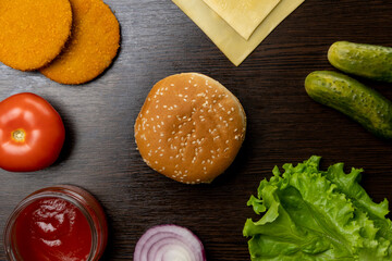 The process of making a burger from different ingredients. Top view. Tomatoes, onions, lettuce leaves, sauce, cutlet, cucumbers, cheese.