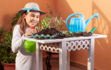 Vista de una niña sonriendo regando con un pulverizador unas pequeñas plantas para el huerto en...