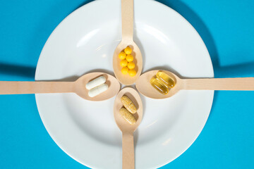 Vitamins on wooden spoons in a white plate on a blue background. Multivitamin set for every day. The importance of obtaining a vitamin complex to improve the functioning of the body and prevent health