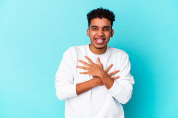 Young african american curly man isolated on blue laughs happily and has fun keeping hands on stomach.