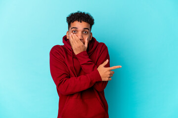 Young african american curly man isolated on blue pointing to the side