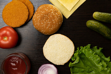 The process of making a burger from different ingredients. Top view. Tomatoes, onions, lettuce leaves, sauce, cutlet, cucumbers, cheese.
