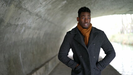Obraz premium young black man walking under bridge wearing scarf and winter coat.