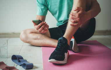 Close up photo of a caucasian man lying on the floor wearing sportswear and chatting on mobile while having a fitness lesson