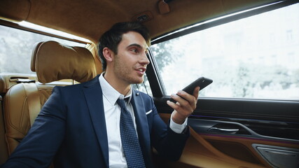 Smiling business man dictating message on smartphone in salon of business car.