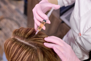 cropped female person at trichologist office get injections in head skin by professional doctor's hands holding disposable syringe under patient's head. Porcedure against hair loss and for skin health