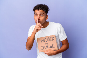 Young african american curly man isolated holding a we need a change cardboard keeping a secret or...
