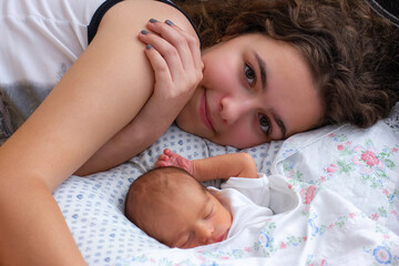 Fototapeta na wymiar Very young mother lays on bed near her sleeping newborn baby