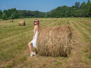 Naklejka na ściany i meble Girl in a field by a bale of hay on a summer day