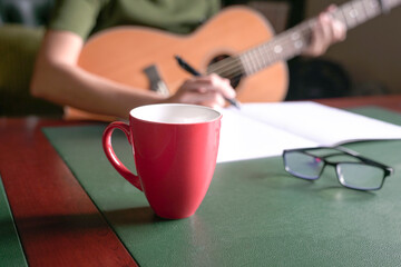 Blur woman musician with guitar writing on book at desk.