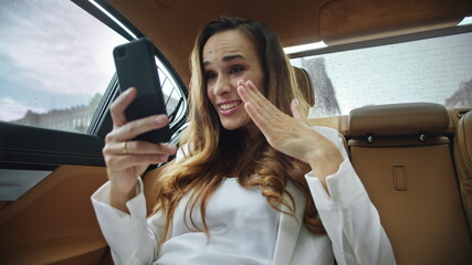 Portrait of happy business lady getting good news on video call in business car.