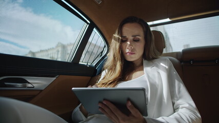 Focused business woman reading data on tablet computer in luxury car.