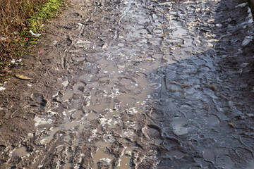 Very dirty pedestrian area with puddles and footprints. Background . The soggy soil of a village road.