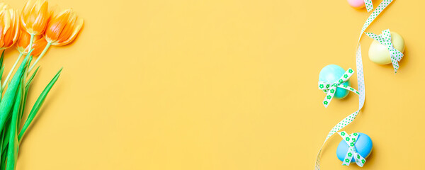 Easter background. Colorful egg with tape ribbon, spring tulips, feathers on pastel yellow background in Happy Easter decoration. Spring holiday top view banner.