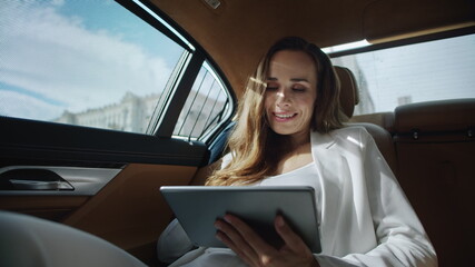 Portrait of smiling business lady working with digital tablet in business car.