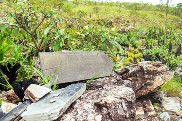 One wooden board indicating the direction to the right, on top of rocks. Path to follow in the woods. Landscape of the Brazilian Cerrado. No writings on the wooden board.