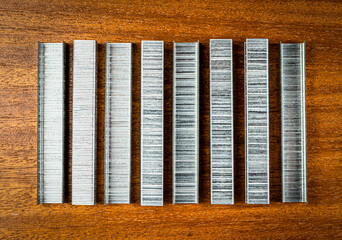 Staplers are stacked in a row on a brown wooden background