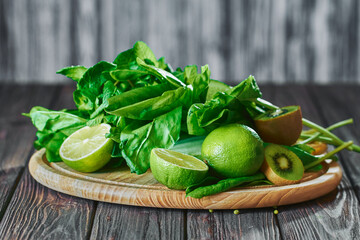 Blended green smoothie with ingredients on the stone board, wooden table selective focus