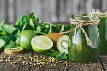 Blended green smoothie with ingredients on the stone board, wooden table selective focus