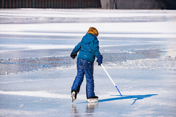 Prague, Czech republic - February 14, 2021. Young boy in blud dress learning ice skating with ice hockey stick in hand