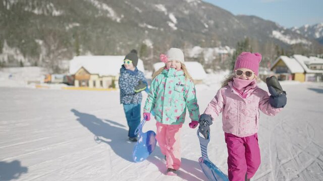 Slow motion - Three toddlers walking uphill in a snow park to go sledding