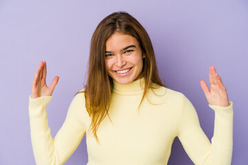 Young skinny caucasian girl teenager on purple background holding something little with forefingers, smiling and confident.